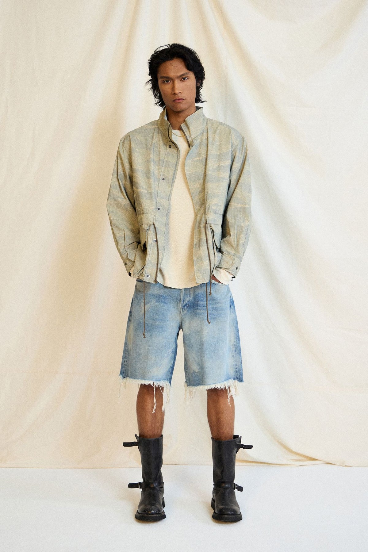 John Elliott Spring 2027 menswear look with faded tiger camo jacket and cut-off denim shorts, image courtesy of John Elliott via Vogue