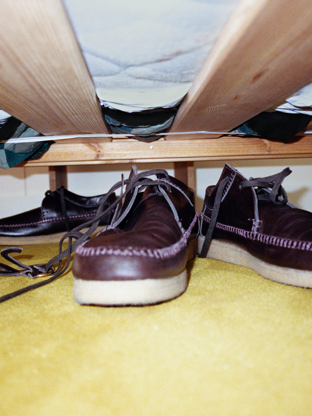 A.P.C. x Clarks Originals campaign — dark brown Weaver / Desert Boot under bed on yellow carpet